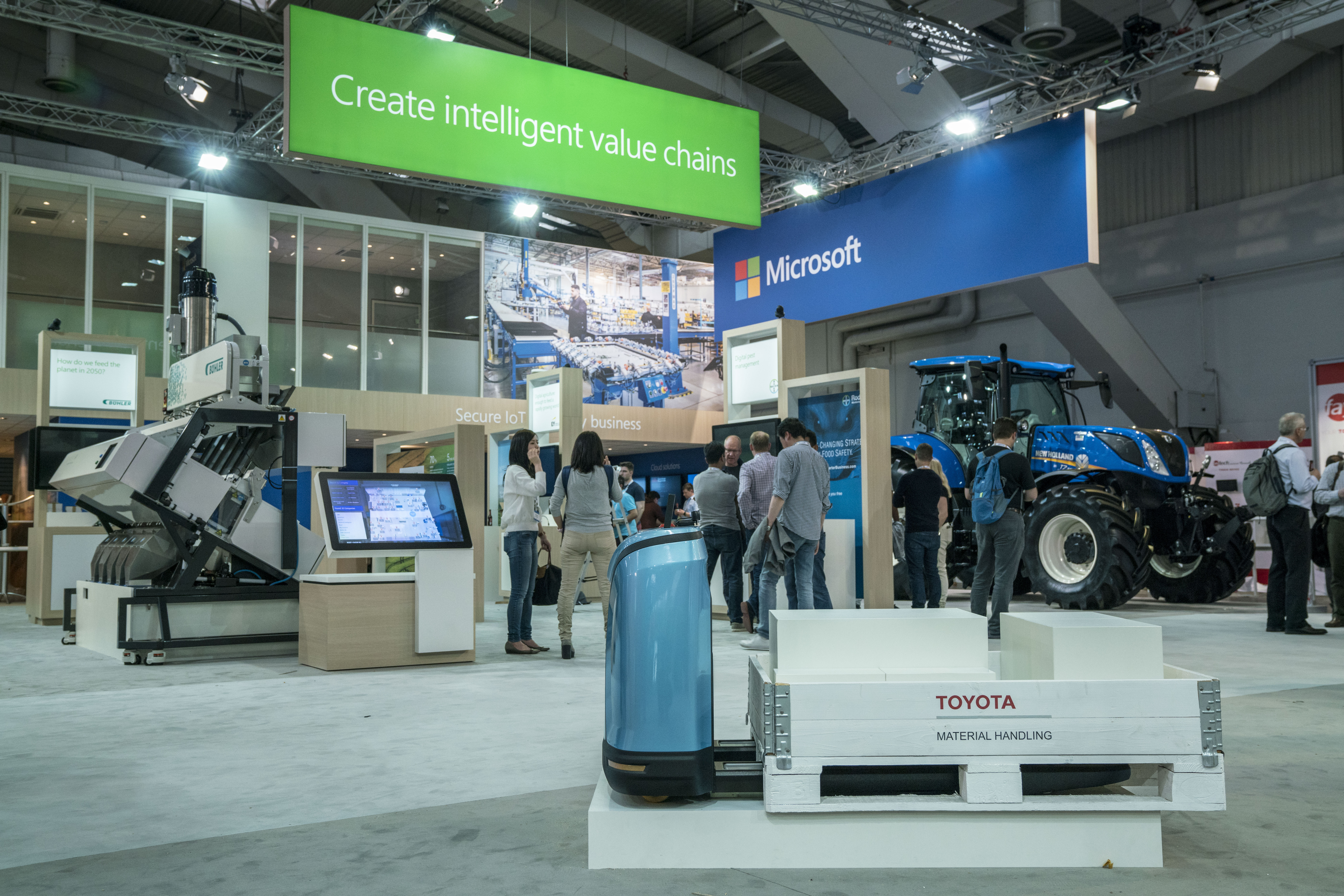 Photo of people crowded under a Microsoft sign surrounded by various technologies including a drone, a food processing machine and a large vehicle