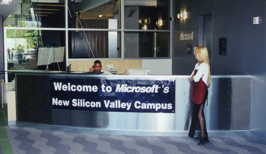 A woman standing at a reception desk that says "Welcome to Microsoft's New Silicon Valley Campus."