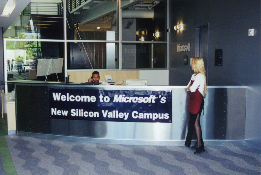 A woman standing at a reception desk that says "Welcome to Microsoft's New Silicon Valley Campus."