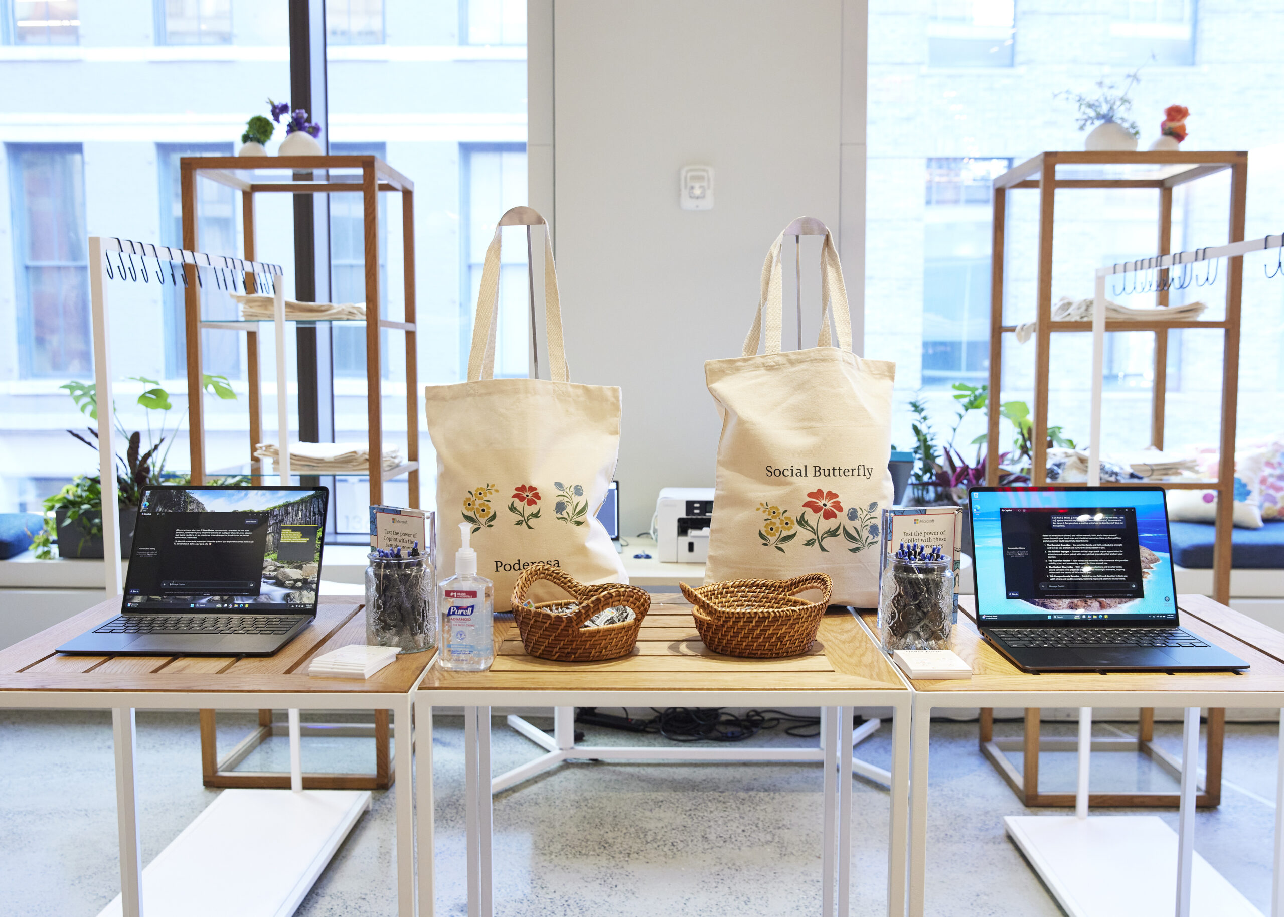 Station for customizing tote bags featuring two printed tote bags and two laptops on a table, with materials for personalization