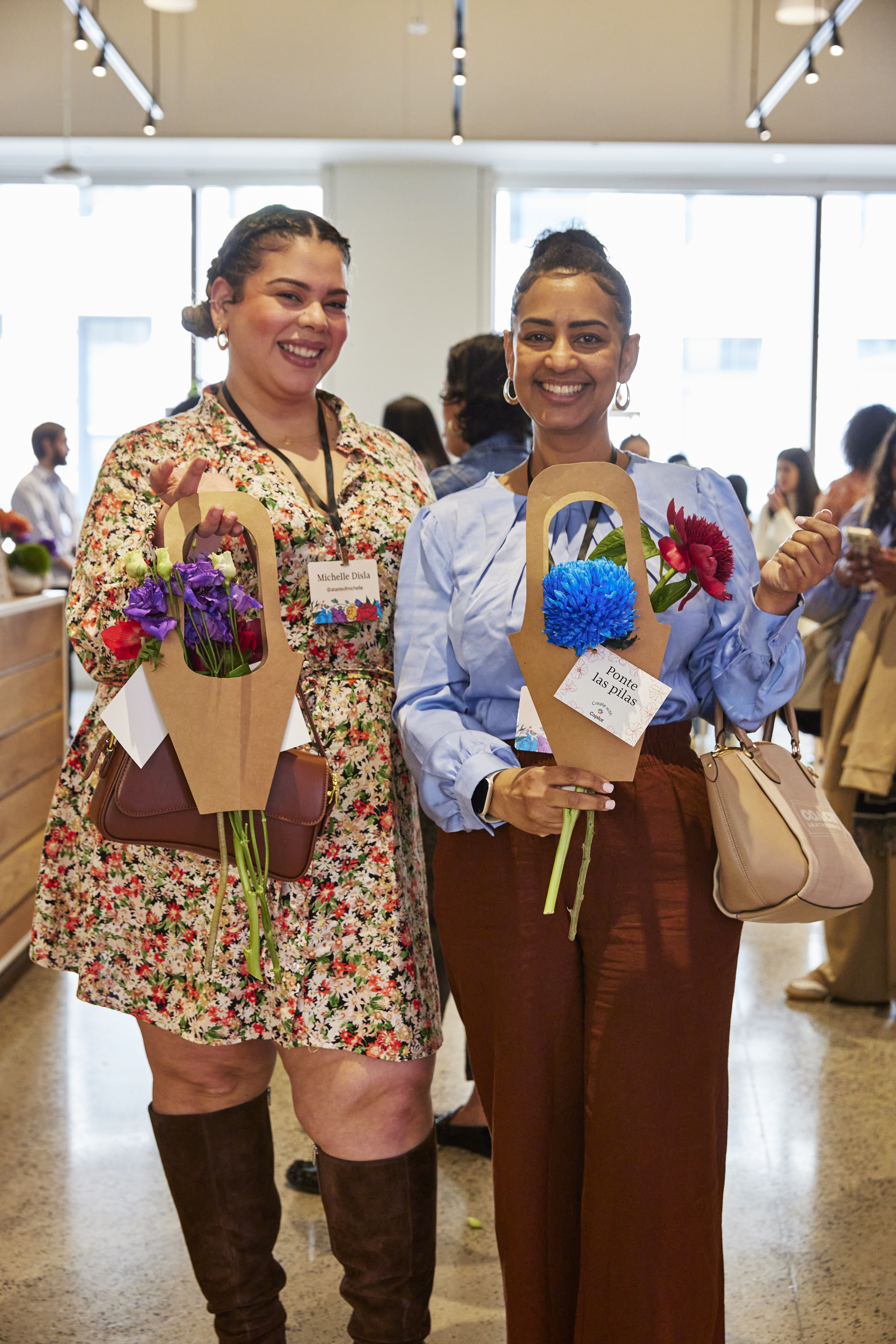 Two individuals holding bouquets of flowers in brown paper holders, standing side by side at an event.