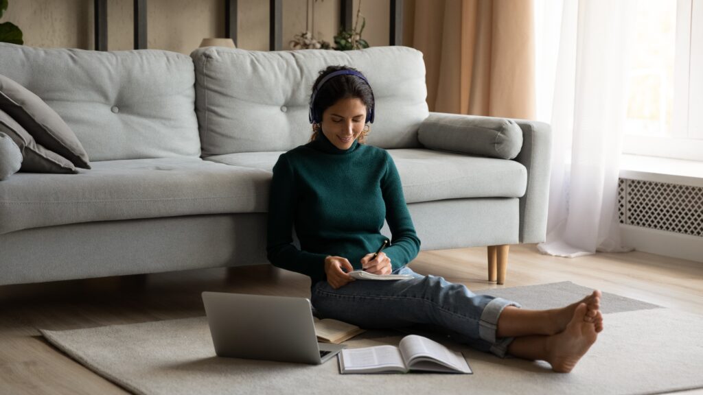 Woman focused on studying, with an open laptop, books and headphones on.