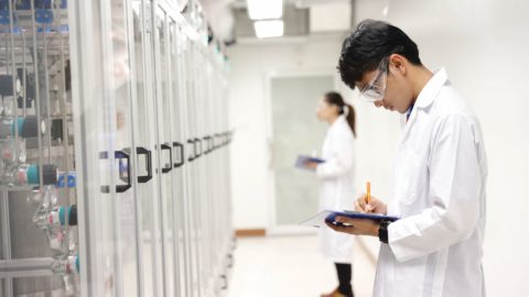 Two individuals in lab coats observe a factory