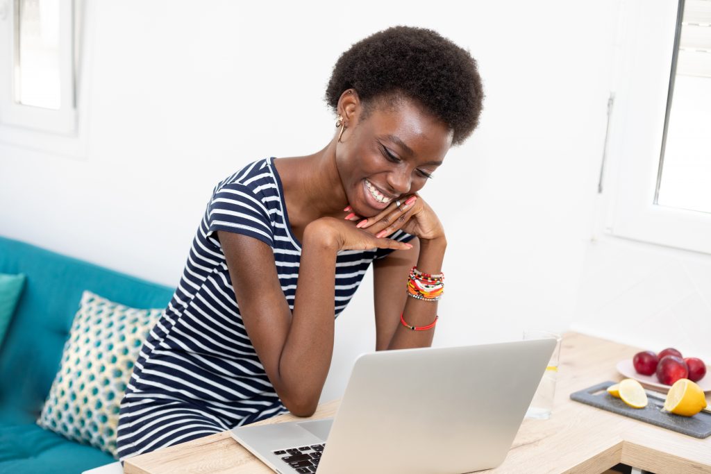 A smiling person sits in front of a laptop