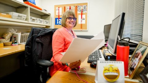 Woman in pink jacket smiling sorting, scanning, and electronically filing mail in an office