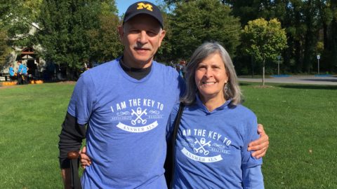 Joel Shamanski and his wife Ann, stand next to each other, outside, at the Answer ALS Walk in Rochester New York. They are both wearing Answer ALS shirts.