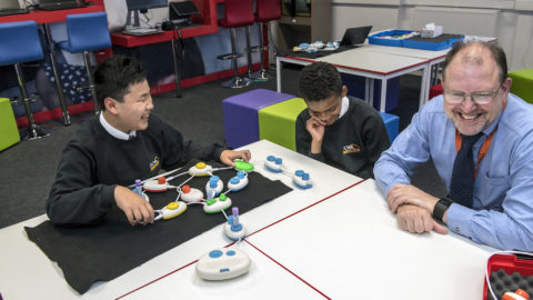 From the left, student Daniel and Rico and IT instructor Jonathon Fogg sit around a table and laugh about the program Daniel and Rico created during a beta test of the technology behind Code Jumper.