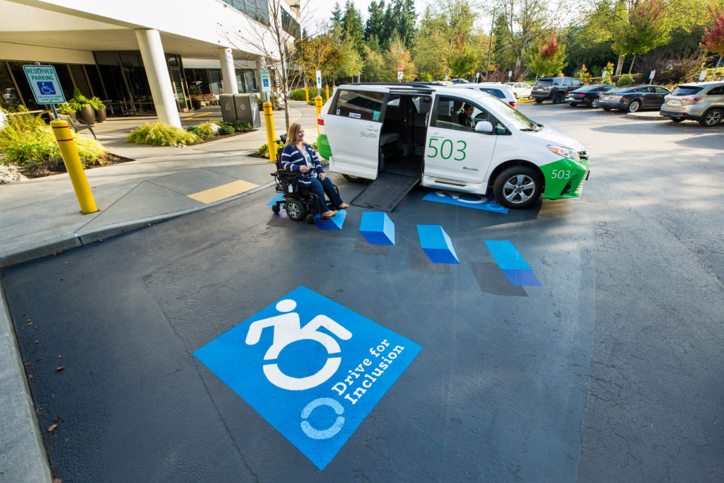 A women in a wheelchair next to a Microsoft shuttle van featuring the new 3-D graphic for ADA Parking spaces at the Living Well Health Center on our Redmond Campus.