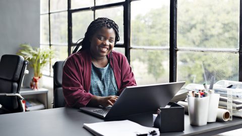 Portrait of smiling businesswoman with disability working on laptop at modern workplace.