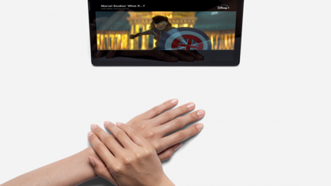 A person with their hands in a relaxed position watching a program on their device.