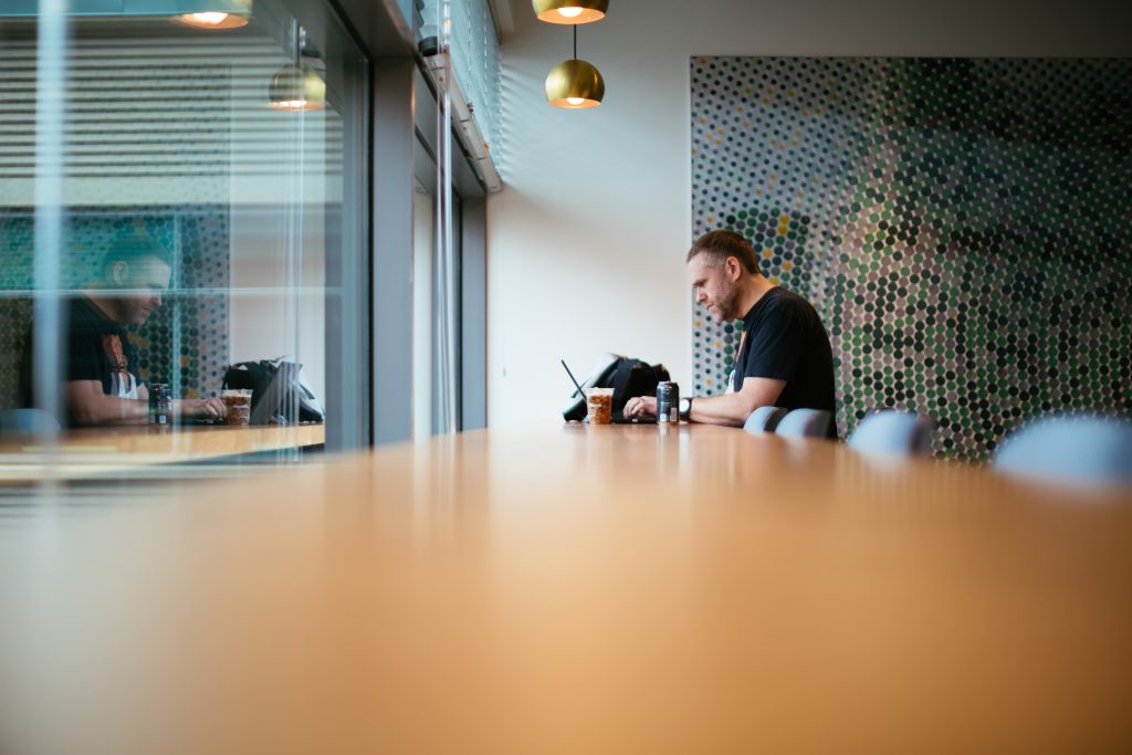 Tobias Brick, a man with a social disability, sits alone in the corner of an office building and works on a laptop. Accessibility, disability, and inclusion collection.