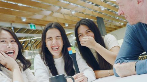 VS Code team members laughing together sitting at a table holding a microphone.