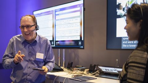 Will Lewis and Amanda Song face each other in front of dual monitors showing real-time translation as the speak