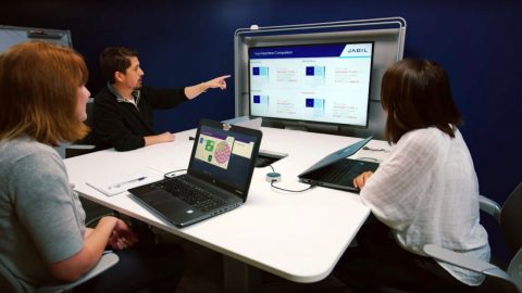 A group of three employees sit at a table interacting with a presentation
