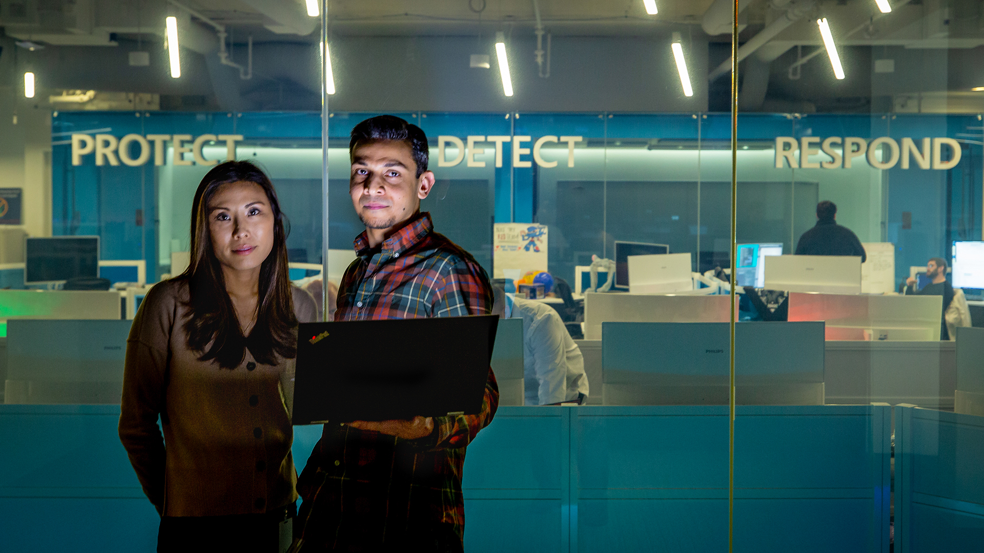 Erin Miyake and Talhah Mir stand in front of a glass partition with an office behind them