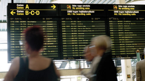 A busy computer terminal with blurry people in the foreground and an arrival/departures board in the background