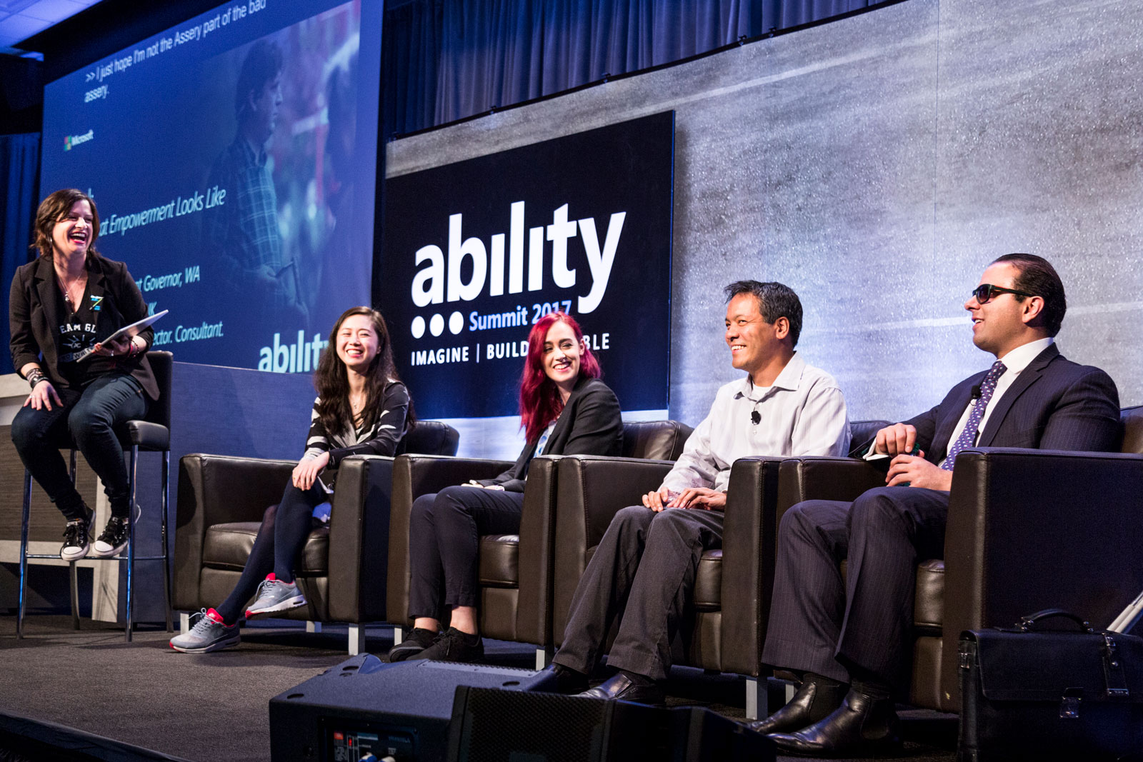 Photo of a host and a panel of four people on stage