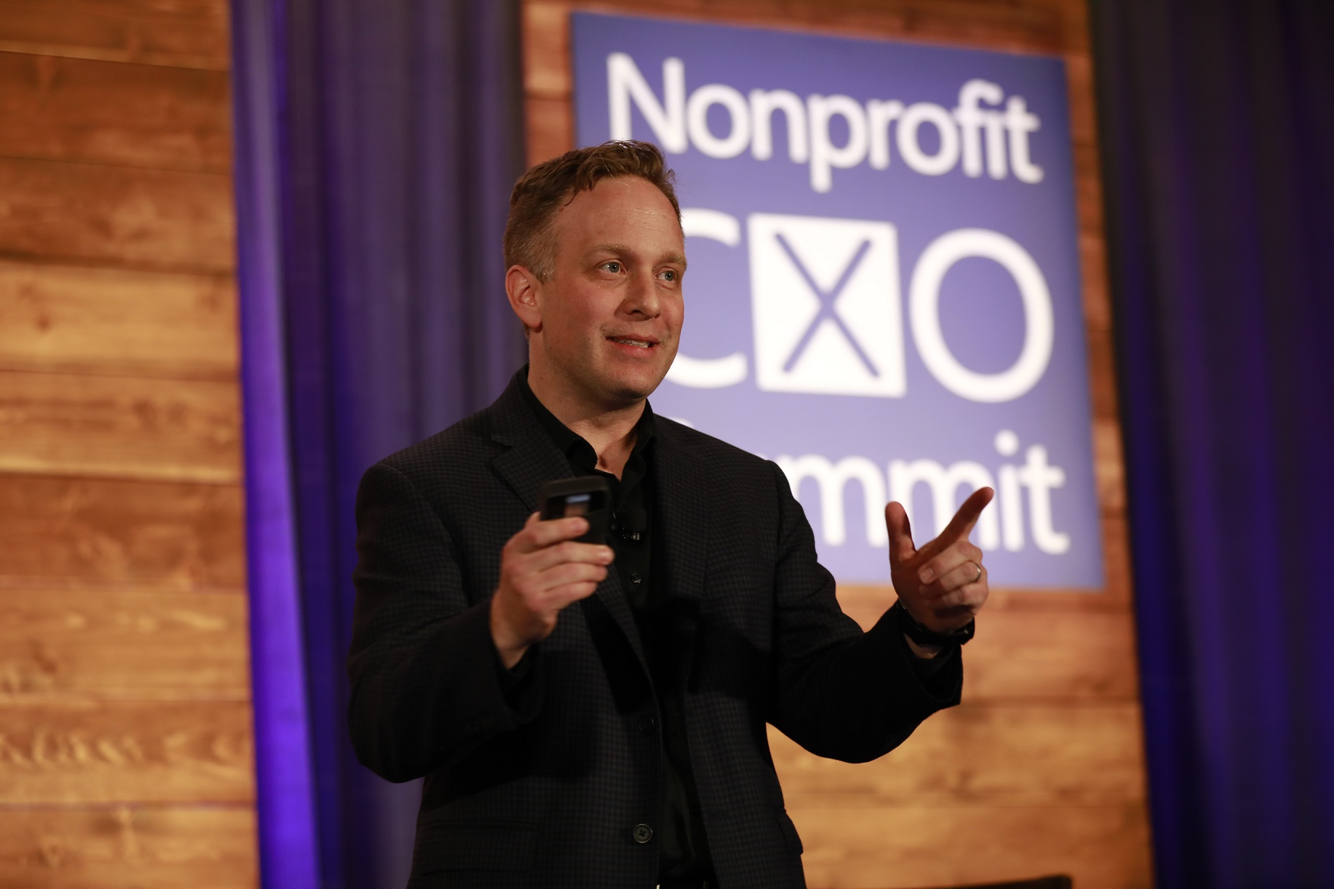 Photo of man on a stage pointing toward the crowd as he gives a speech