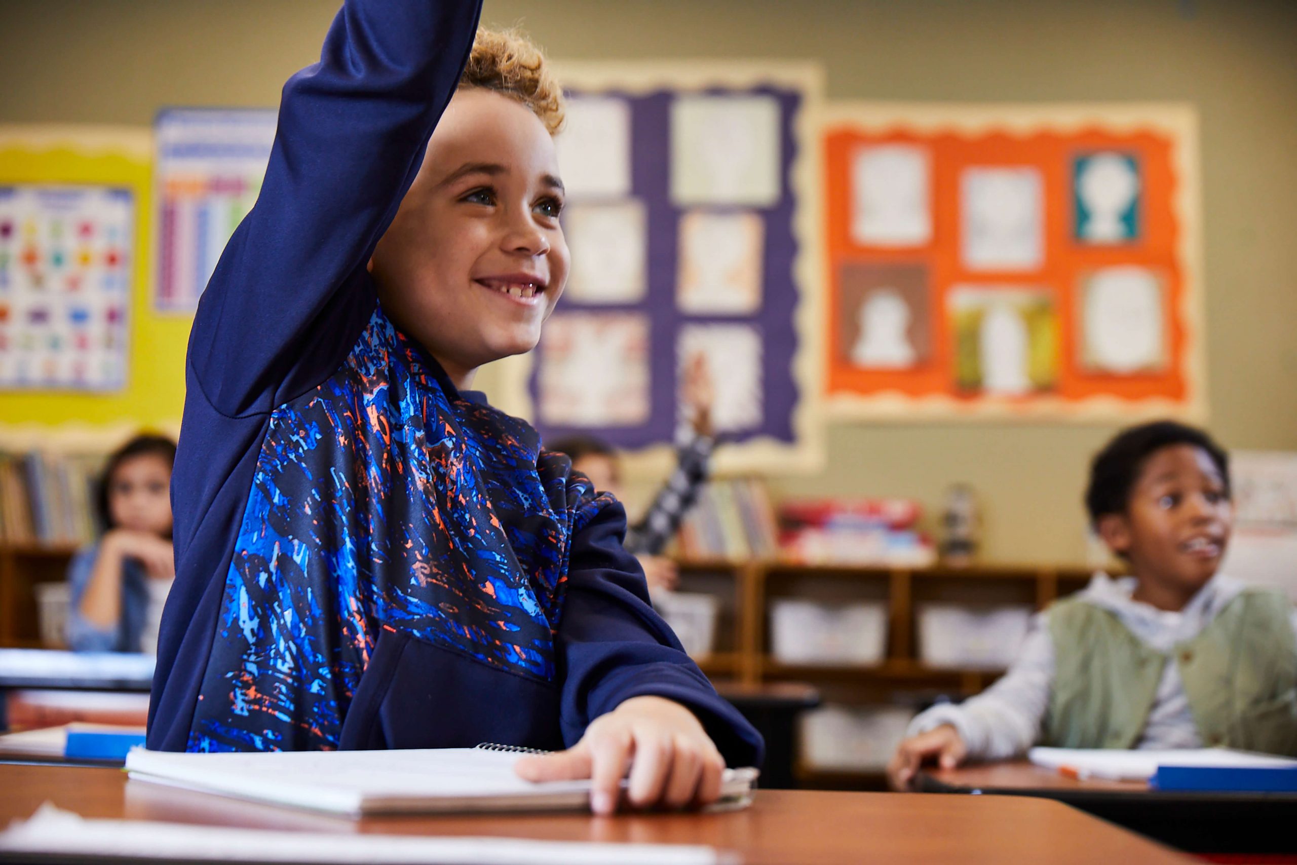 Young boy in class raises his hand