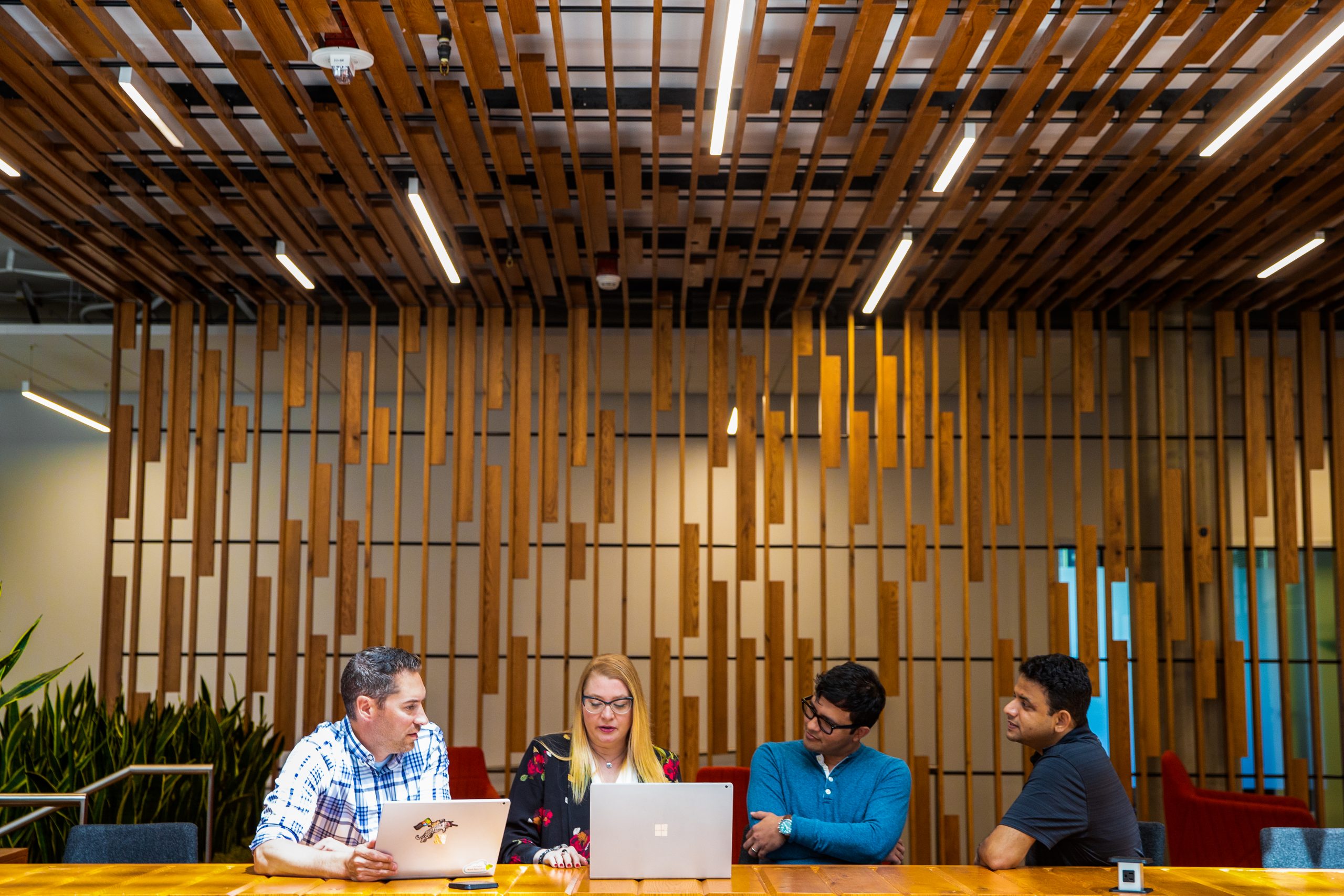 Four employees sitting at a table in an office environment, all looking at a laptop.