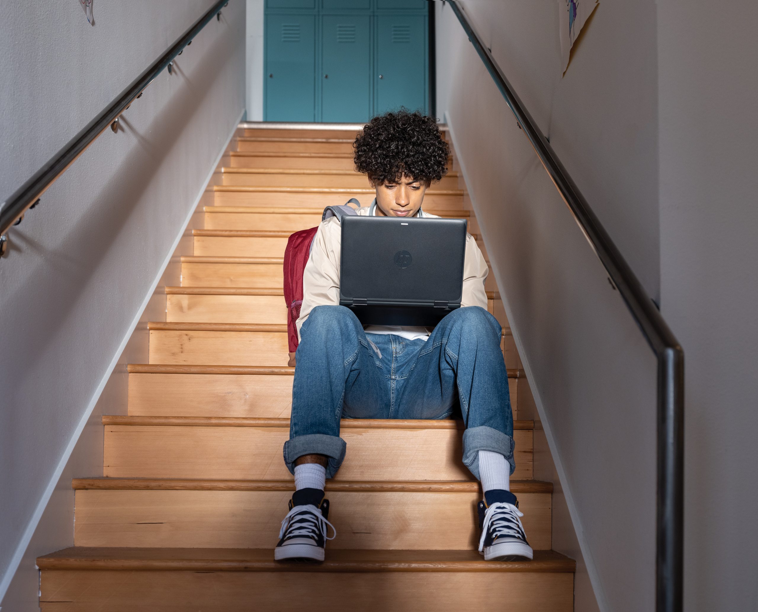 a young person sits on stairs using their laptop