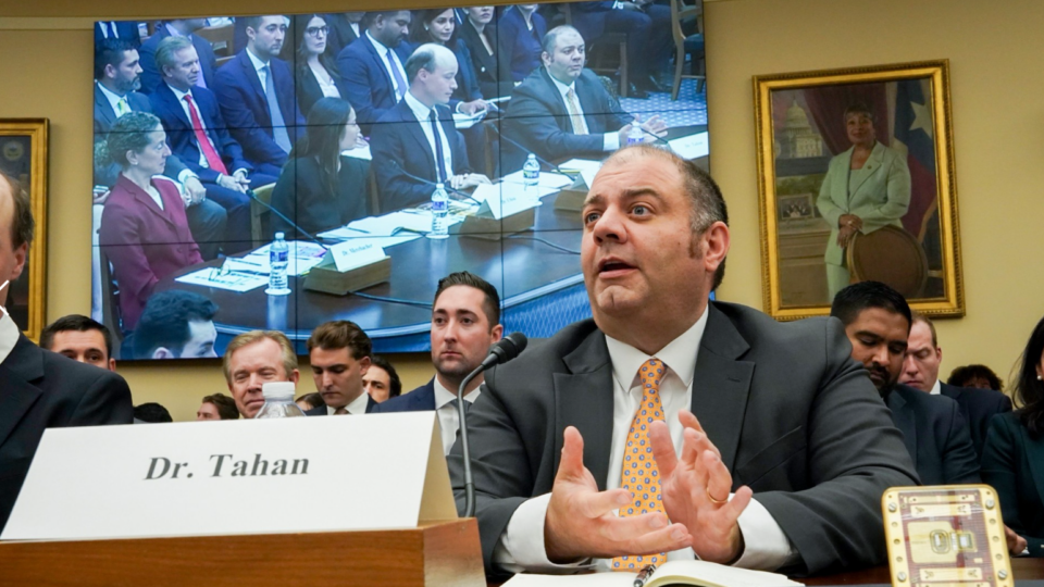 Congress meeting with Dr. Tahan speaking at a long table, joined by others in person and on a large screen in the background, in a room with framed portraits.
